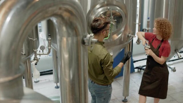 Man and woman working in craft brewery checking quality of a beer