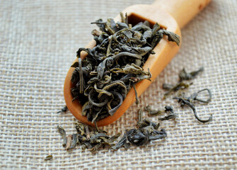A wooden spoon with leaf tea lies on a jute bag.