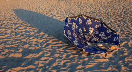 Blue beach umbrella upside down. Solitude of a summer afternoon. Parasol. Shadows that stretch on the beach. Sunlight.
