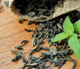 Jute bag with leaf tea and fresh mint leaves lying on a wooden background.