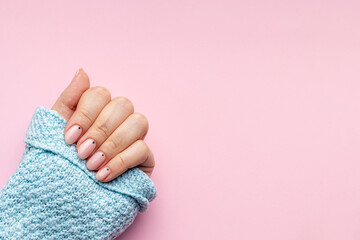 Female hand in a blue knitted sweater fabric with trendy beautiful manicure - pink nude nails with...