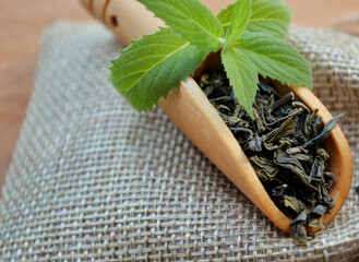 Wooden spoon with leaf tea and fresh mint leaves lies on a jute bag.