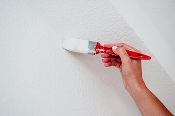 close up of caucasian woman painting the room walls with white color. Do it yourself and new home concept