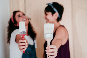 happy lesbian couple painting the room walls with white color. Do it yourself and new home concept
