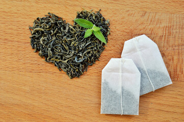 Heart made from loose leaf tea, tea bags and fresh mint leaves on wooden background