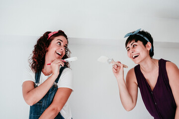 happy lesbian couple painting the room walls with white color. Do it yourself and new home concept