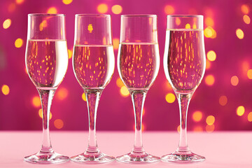 Four champagne glasses against pink background with blurred garland