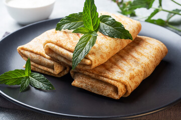 Stuffed thin pancakes rolled into rolls are grilled on a black plate with mint.