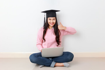 Young attractive Asian woman sitting with laptop on her legs wearing graduated hat, online education class, scholarship study abroad concept.