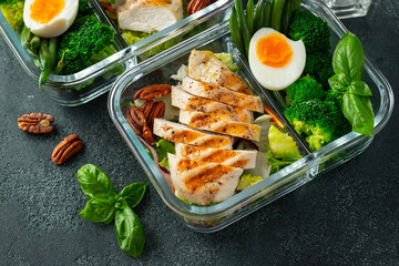 Healthy meal prep containers with green beans, chicken breast and broccoli. A set of food for keto diet in lunchbox on a dark concrete background. Top view