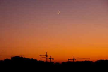 Evening sky over the city Kaliningrad. You can see the moon and cranes on the background of a beautiful sunset.