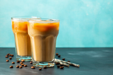 Ice coffee in a tall glass with cream poured over and coffee beans on a light stone background....