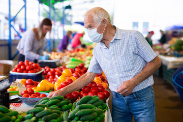 retired european man wearing medical mask protecting against the virus buying cucumbers and tomatoes in market