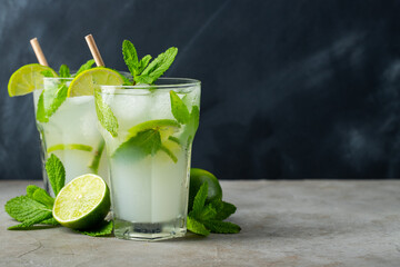 Two homemade lemonade or mojito cocktail with lime, mint and ice cubes in a glass on a dark stone...