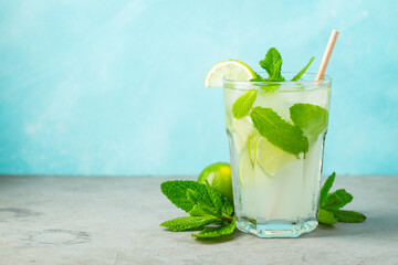 Two homemade lemonade or mojito cocktail with lime, mint and ice cubes in a glass on a light stone table. Fresh summer drink. With copy space.