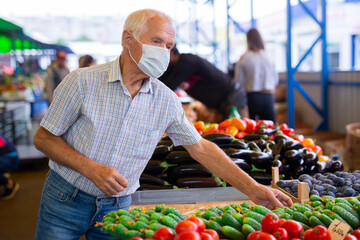 Fototapeta premium retired european man wearing medical mask protecting against virus buying tomatoes in market