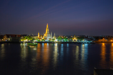 Fototapeta na wymiar The illuminated temple of Wat Arun on the Chao Phraya river at sunset/night in Bangkok, Thailand