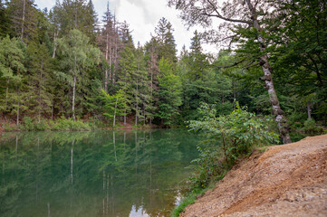Fototapeta na wymiar Natural colorful lakes in Europe. Kolorowe Jeziorka in Rudawy Janowickie, Poland. Beautiful turquoise lake with reflection against forest.