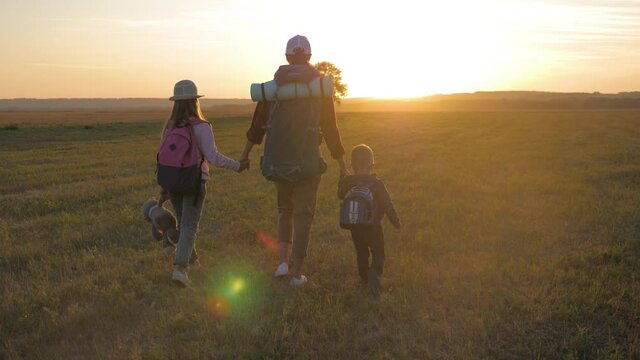 Mother and two children walking in the meadow at the sunset time. Silhouette happy beautiful family during the travelling. Concept of friendly family and travel.