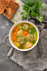 Soup with meatballs in a white bowl. Dark background, gray linen napkin. Healthy meatball soup with parsley, carrots and noodles. Top view.