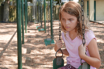 Sad girl sitting alone on a swing in a playground