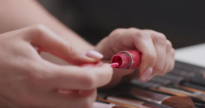 Makeup artist applying red lip gloss on hand skin, close up
