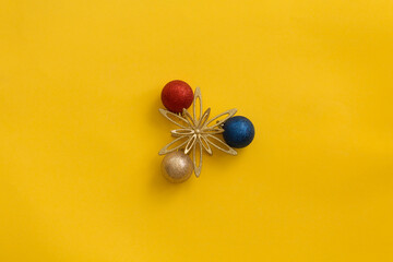 Three Christmas shiny balls and a star on a bright yellow background close-up.