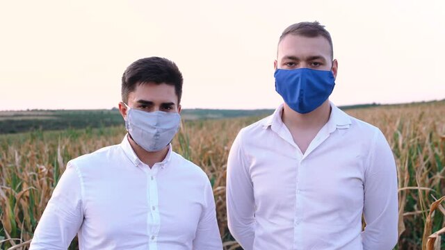 Portrait of two disappointed farmers wearing protective masks in a cornfield severely affected by drought. The drought of 2020 affects cereal crops.