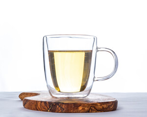 Glass cup of hot green tea on wooden stand on white background.