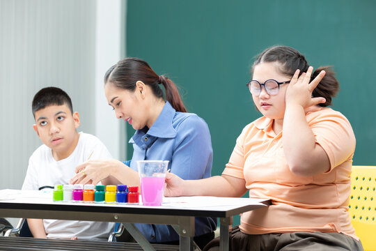 asian disabled kids or autism child learning and painting at paper with teacher helping in classroom