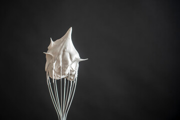 Metal whisk with whipped egg whites on black background