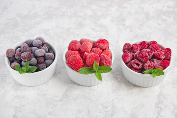 Frozen raspberries, blueberries and strawberries in bowls on a gray concrete background. Storage and use of frozen products