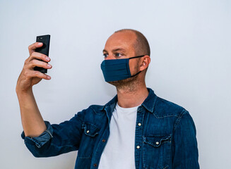 Man wearing a custom design face mask takes a selfie with his mobile phone.