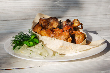 Grilled meat laid out on a plate in pita bread with herbs and fresh onions.