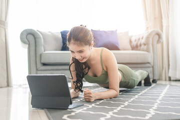 A sporty woman in sportswear exercises while watching online exercise session on her smart phone at home