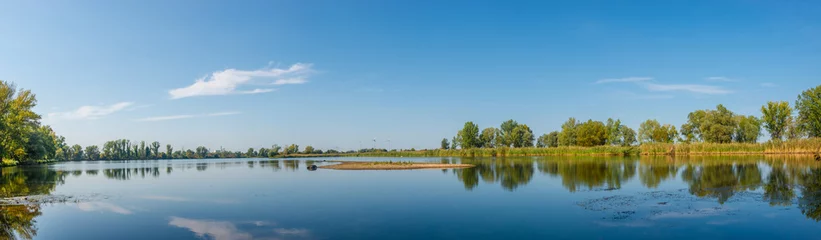 Panoramablick über einen See in der Nähe der Elbe mit Windkraftanlagen am sonnigen Tag und blauem Himmel, Magdeburg, Deutschland. © neurobite