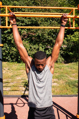 Fototapeta premium Handsome fit African American young man doing pull-ups on chin-up bar during workout outdoors