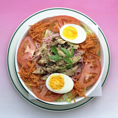 Ensalada de atún con tomate zanahoria lechuga huevo duro y perejil, fondo rosa degradado.