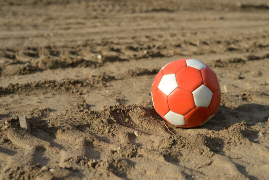 Used soccer ball in red and white on dirth earth