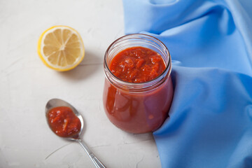 Harissa spicy seasoning in a glass jar, lemon, spices in a spoon and a blue napkin on a white background.