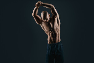 young bodybuilder look down isolated on black stretch his arms above his head while posing and...
