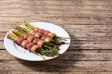 Green asparagus wrapped with bacon on wooden table.Copy space