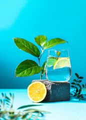 A glass of water with lemon and mint on pedestal in fashion trendy style on a blue background.