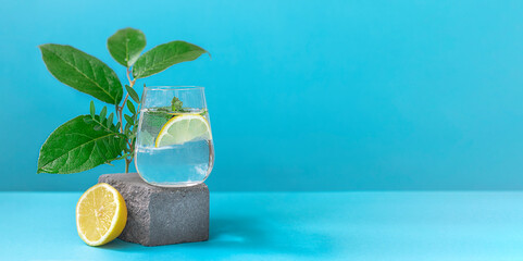 A glass of water with lemon and mint on pedestal in fashion trendy style on a blue background....