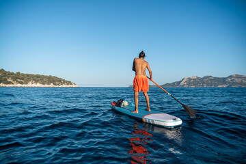 Fototapeta na wymiar Young spanish man using his SUP on an idyllic place in Formentor, Mallorca (Spain) during a sunny day