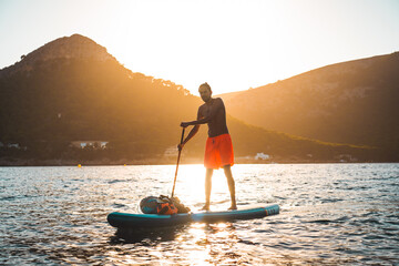 Young spanish man using his SUP on an idyllic place in Formentor, Mallorca (Spain) during sunset