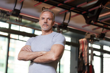 Portrait of mature muscular instructor standing with his arms crossed and looking at camera in the gym