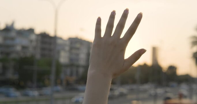 Waving hand to glare of sun flare in afternoon time, urban street. Woman's hand on urban street, sunbeams an gesture.