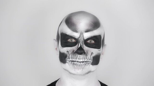 Cheerful funny man in skeleton make-up for Halloween smiles at the camera. Shooting in the studio. Gray background