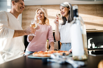 Happy man and two women with wine glasses on the kitchen